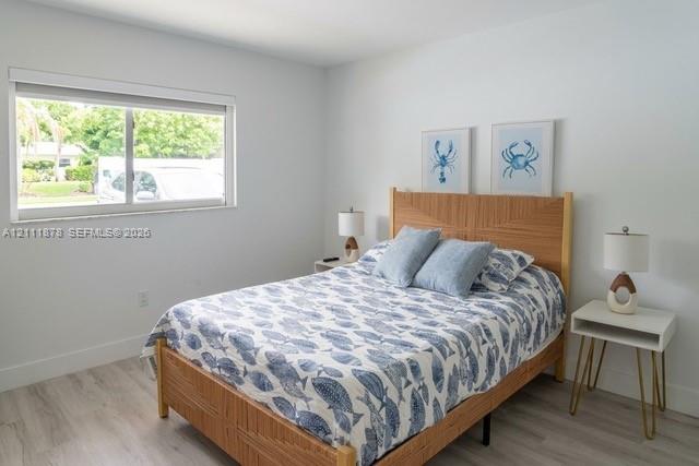 Bedroom interior featuring wood-finish flooring, a neutral color palette, and a large sliding window with a minimalist blind Bedroom interior featuring wood-finish flooring, a neutral color palette, and a large sliding window with a minimalist blind