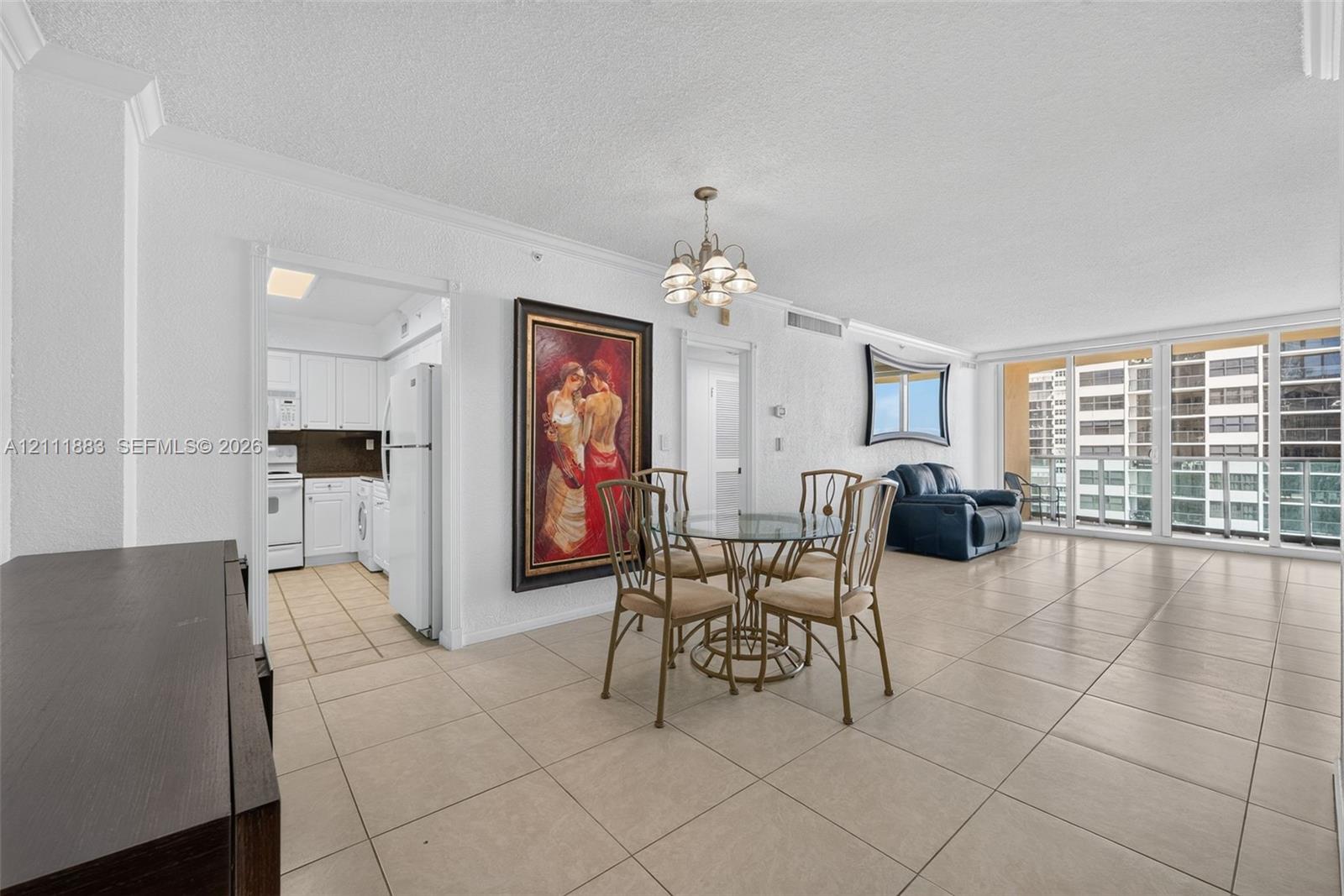 Open-concept interior featuring large-format ceramic tile flooring, a multi-light chandelier, floor-to-ceiling glass sliding doors, and crown molding