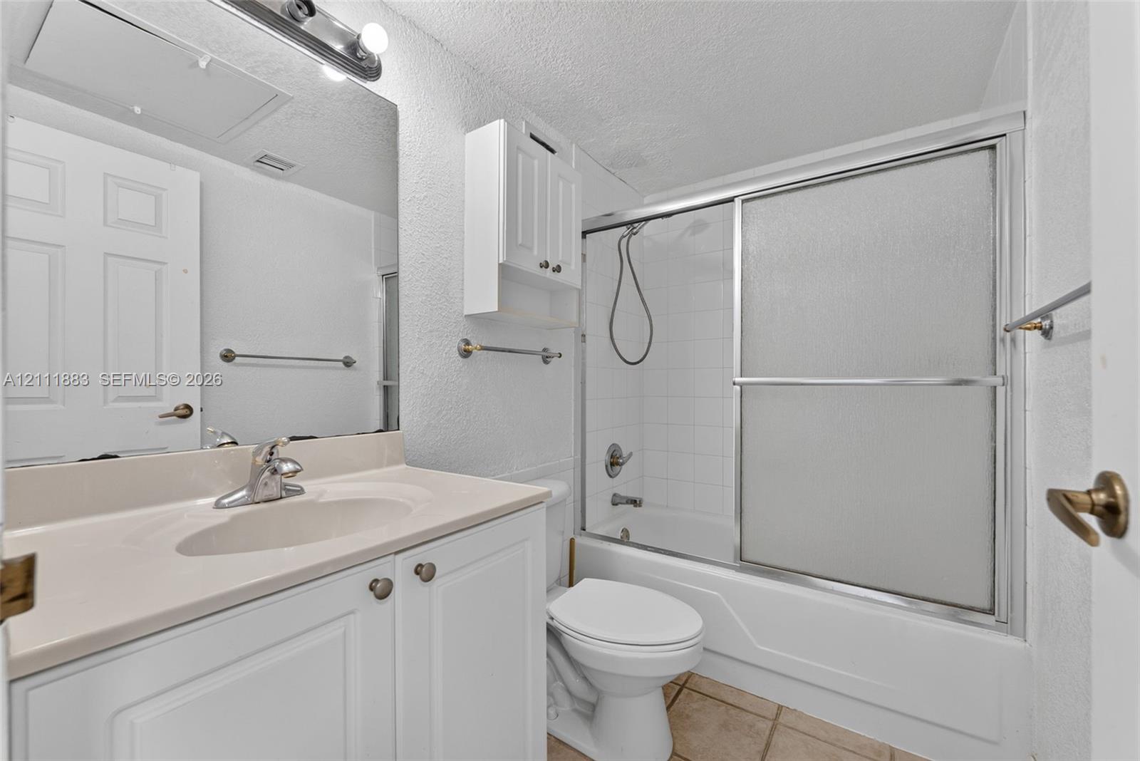 Bathroom featuring a white vanity cabinet with an integrated basin, wall-mounted storage cabinetry, a large vanity mirror with overhead lighting, and a tub-shower combination with sliding glass doors