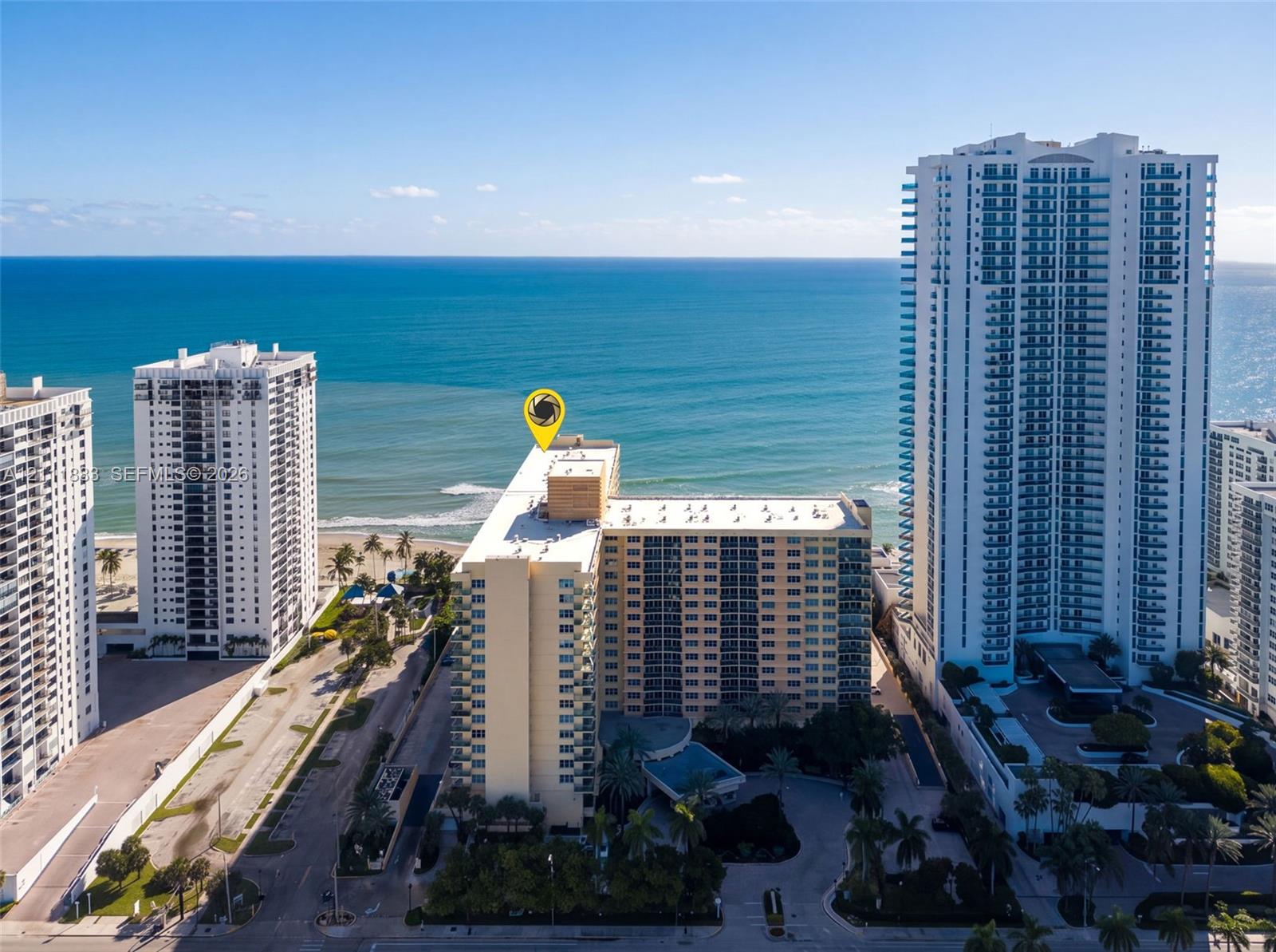High-rise residential building featuring expansive ocean frontage, private balconies, structured parking, and palm tree-lined landscaping