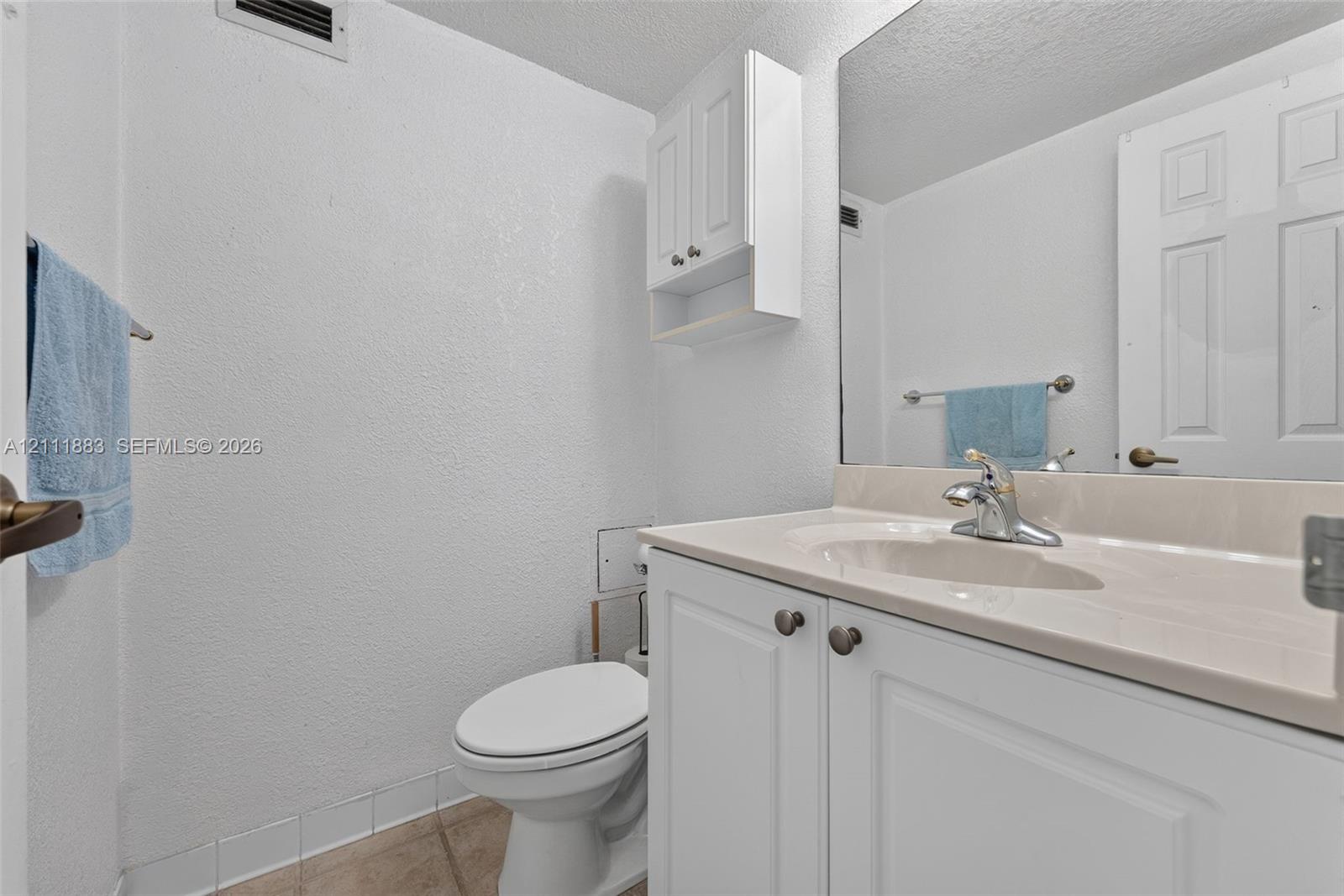 Bathroom featuring a white vanity cabinet, solid-surface countertop with integrated sink, chrome-finish faucet, wall-mounted storage cabinet, and large-scale mirror