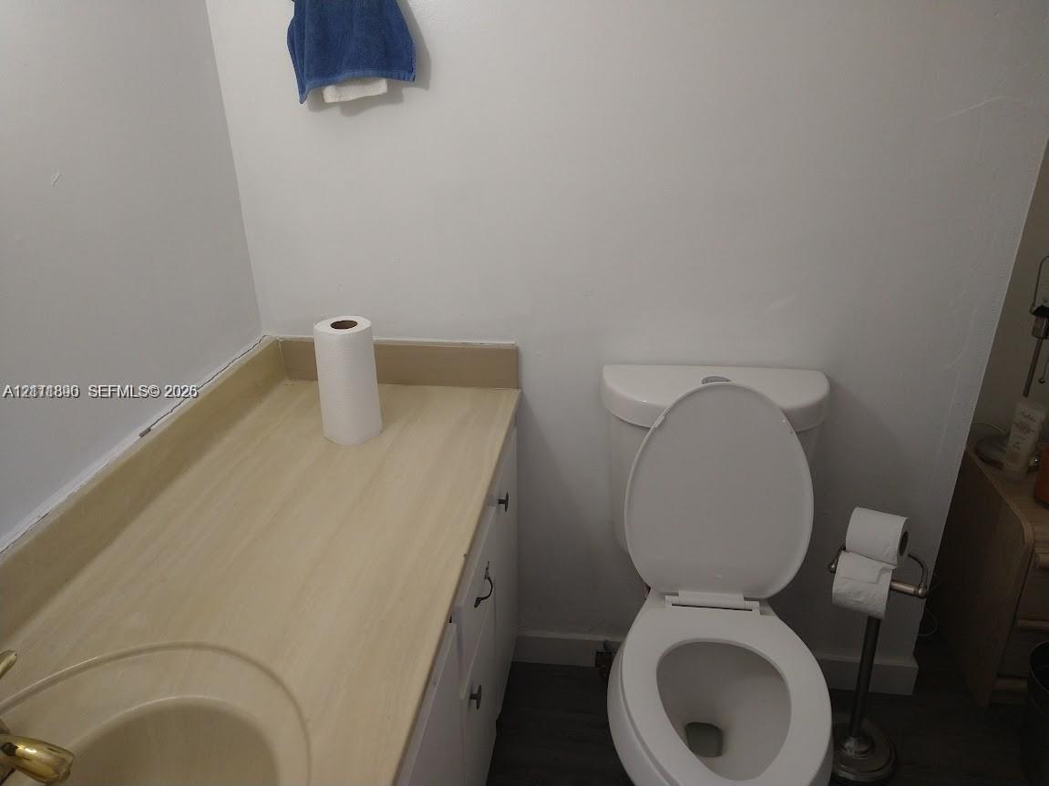 Bathroom featuring a vanity with a laminate countertop, integrated sink, and white cabinetry paired with a standard two-piece toilet