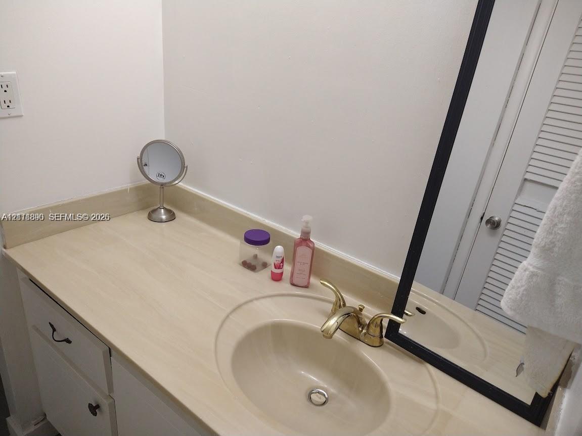 Bathroom vanity featuring a solid-surface countertop with an integrated basin, brass-finish double-handle faucet, white cabinetry, and a rectangular mirror with a black frame