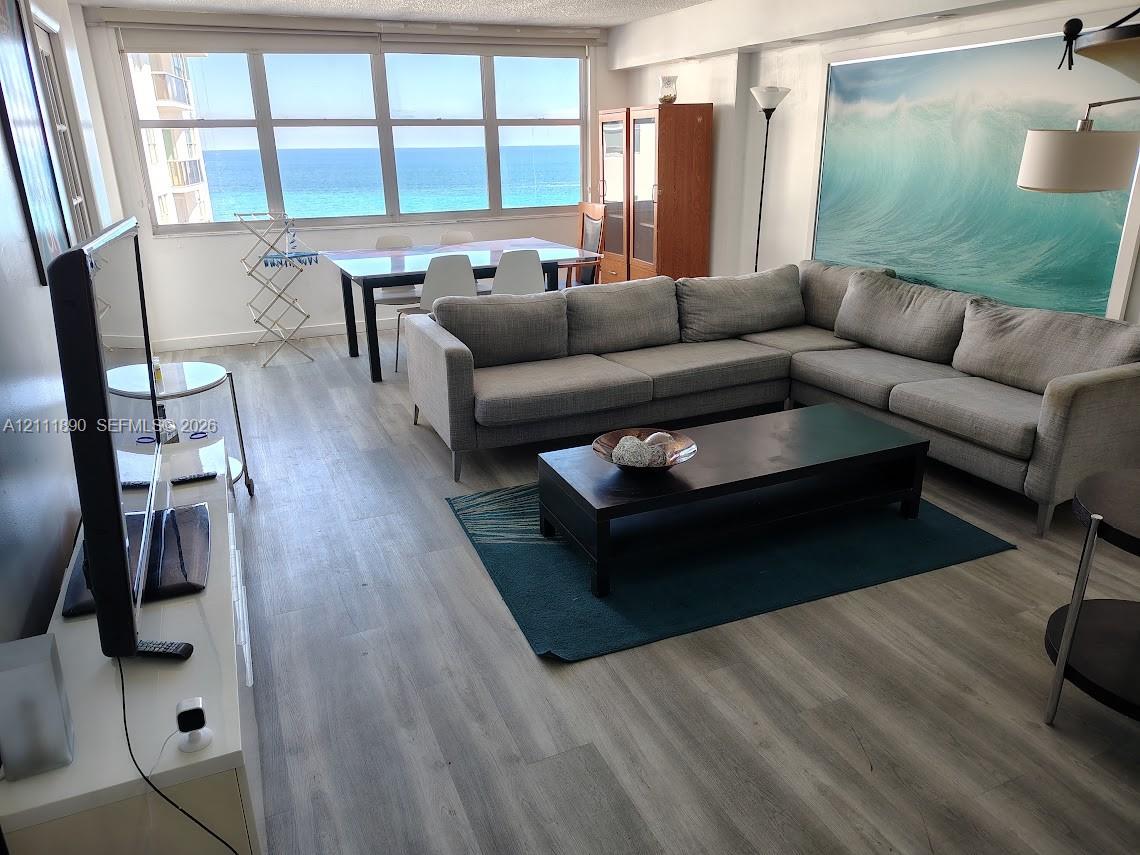 Open-concept living space featuring wood-finish flooring and a expansive wall of windows with an ocean backdrop Open-concept living space featuring wood-finish flooring and a expansive wall of windows with an ocean backdrop