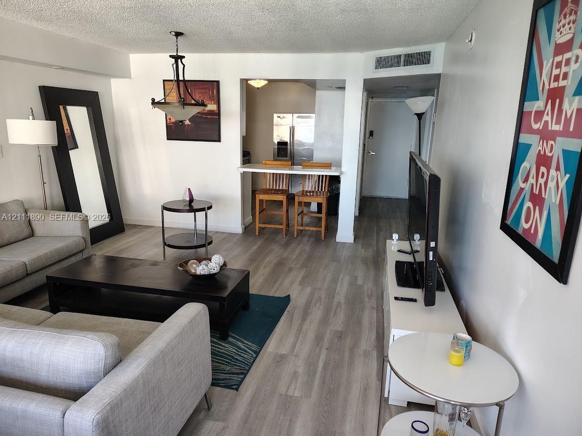 Open-concept floor plan featuring wood-finish flooring, a built-in breakfast bar, and a hanging metal chandelier Open-concept floor plan featuring wood-finish flooring, a built-in breakfast bar, and a hanging metal chandelier