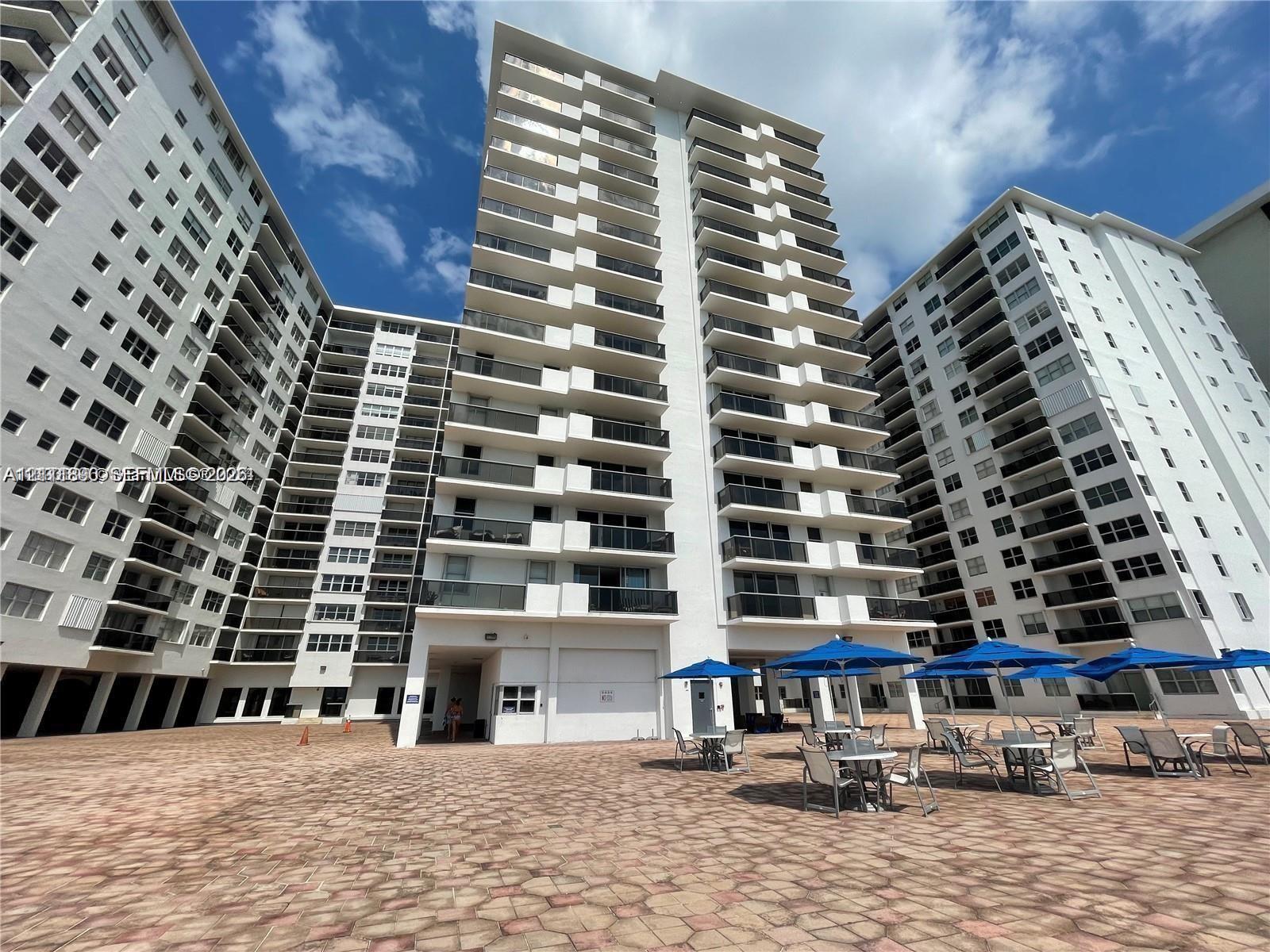 High-rise residential exterior featuring stacked private balconies, neutral facade, and a paved stone courtyard