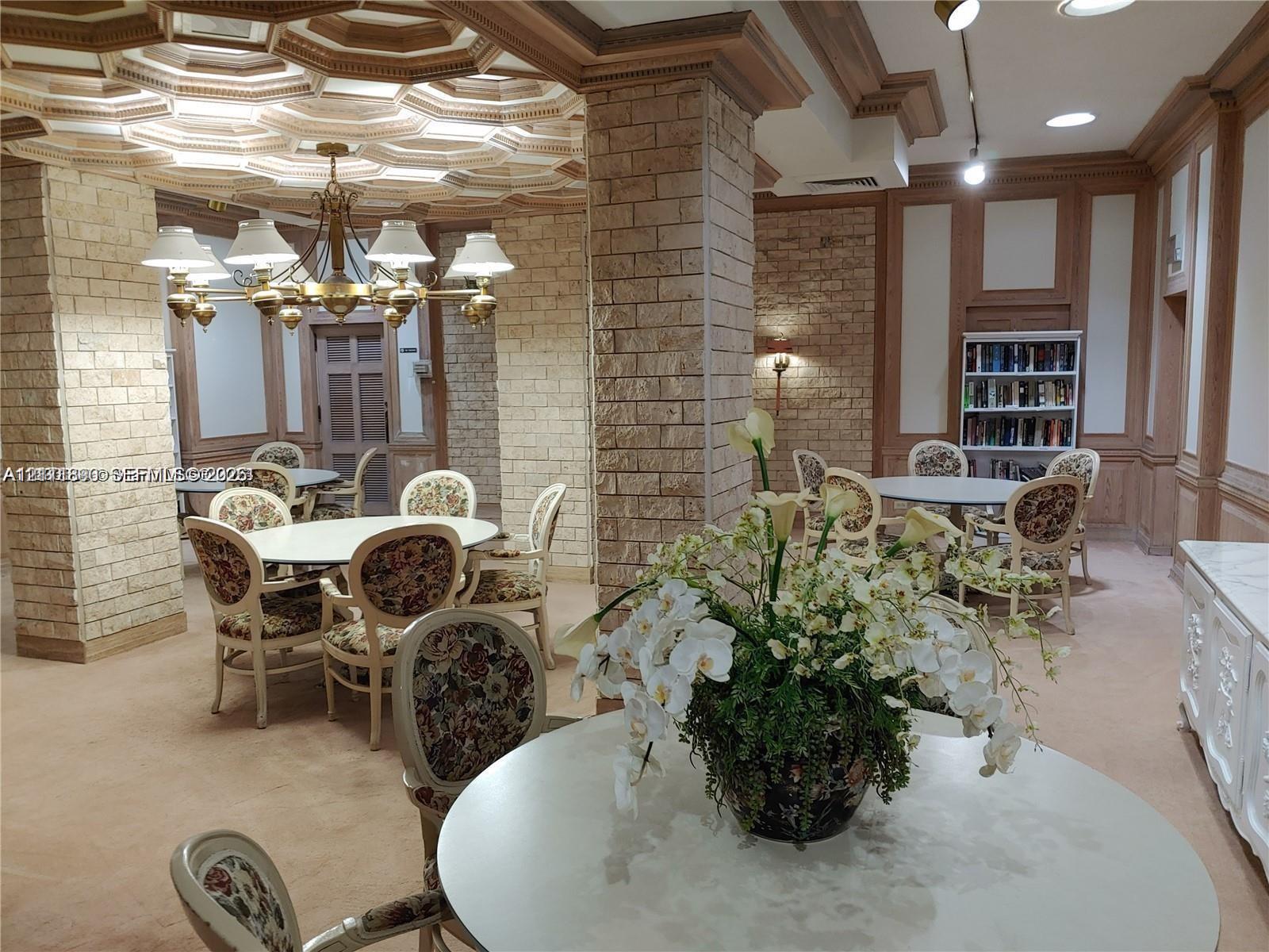 Intricate coffered ceiling, exposed stone columns, custom wood wall paneling, built-in shelving, and tiered brass chandelier