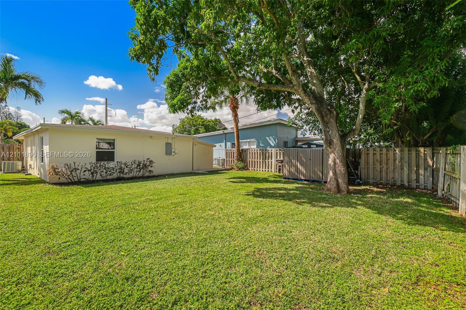 Expansive backyard featuring a large grass lawn, mature trees, and perimeter wood privacy fencing