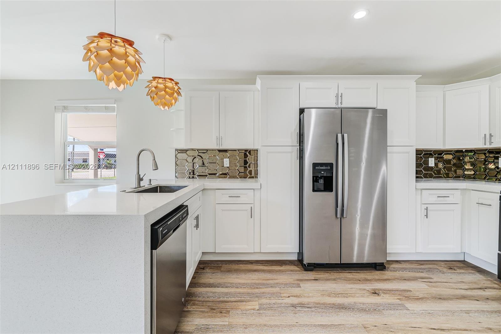 Kitchen featuring white cabinetry, solid-surface countertops, stainless steel appliances, geometric-patterned backsplash, and wood-finish flooring Kitchen featuring white cabinetry, solid-surface countertops, stainless steel appliances, geometric-patterned backsplash, and wood-finish flooring