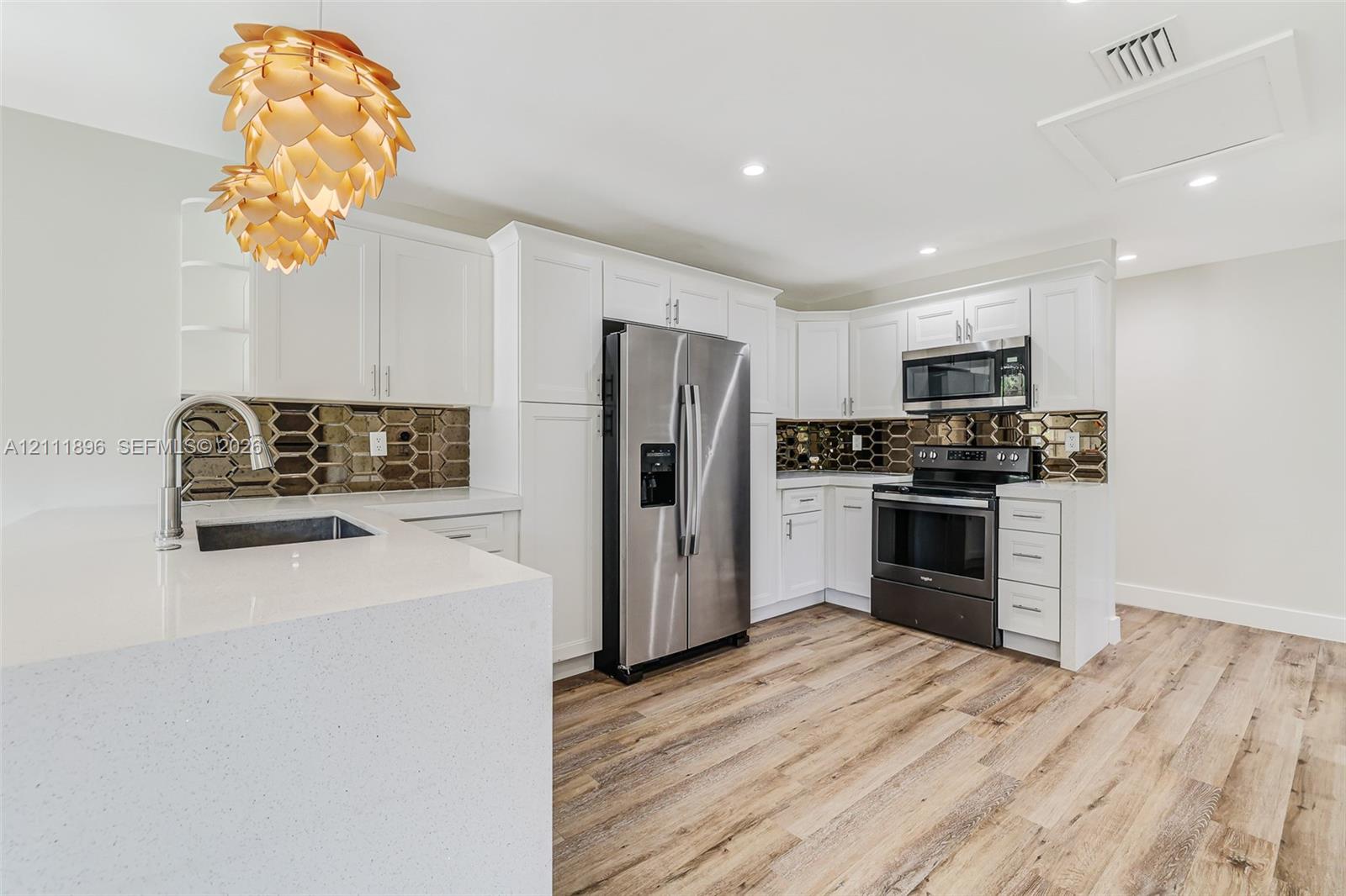 Kitchen featuring white shaker-style cabinetry, quartz countertops, stainless steel appliances, geometric metallic backsplash, and wood-finish flooring