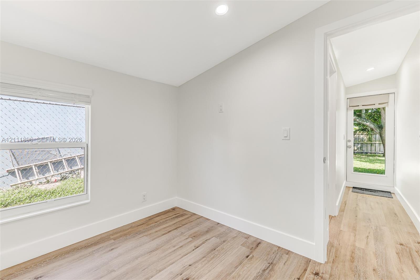 Neutral interior featuring wood-finish flooring, recessed lighting, a single-pane window with custom blinds, and a glass-panel exterior door