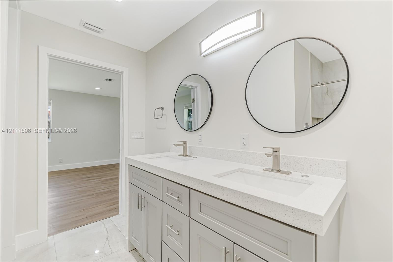 Double vanity featuring gray shaker-style cabinetry, a stone-composite countertop, integrated rectangular sinks, brushed-nickel faucets, and dual circular mirrors