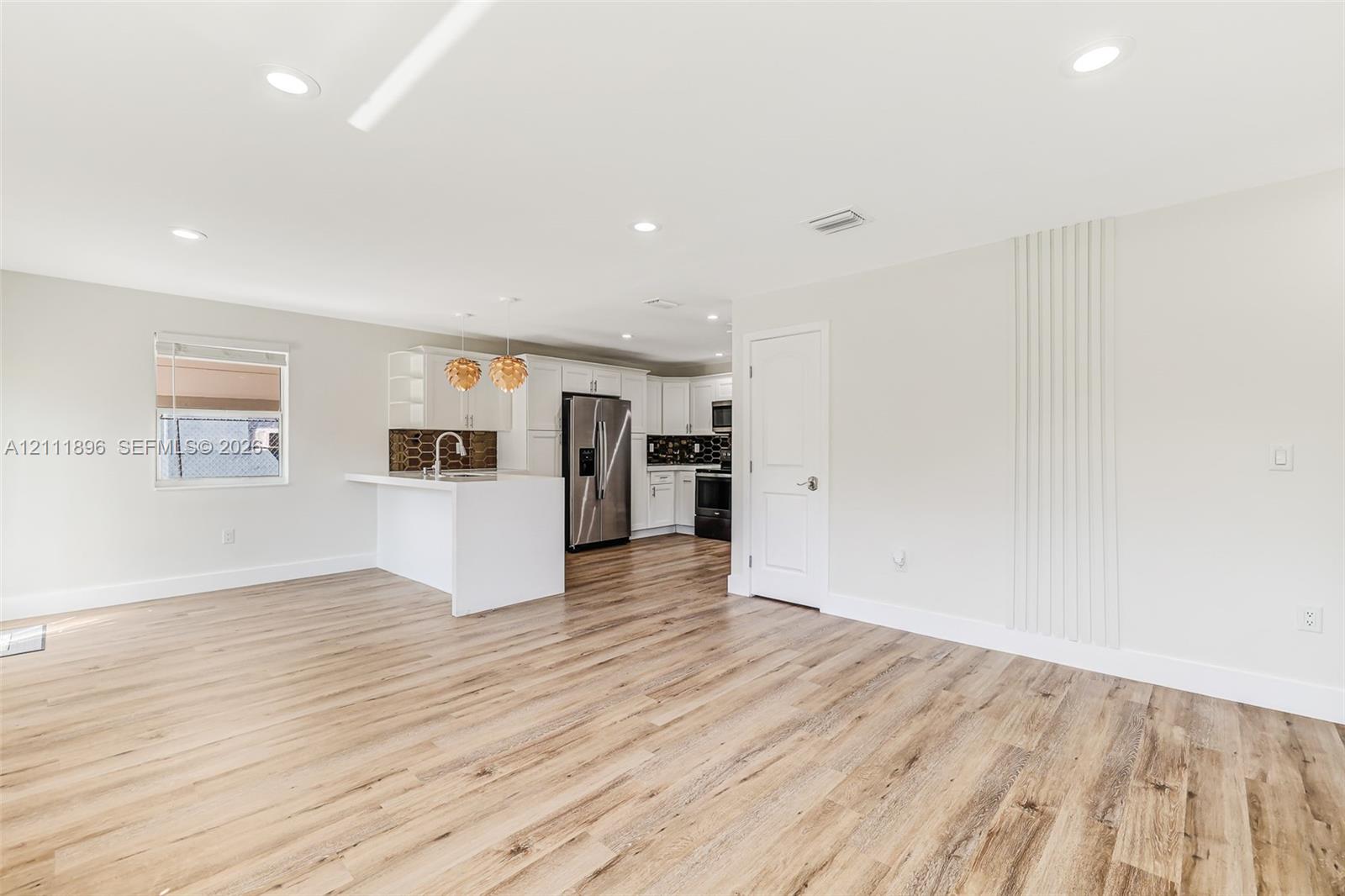 Open-concept space featuring wood-finish flooring, recessed lighting, white cabinetry, a kitchen island with a stainless steel faucet, and a decorative vertical-slat accent wall