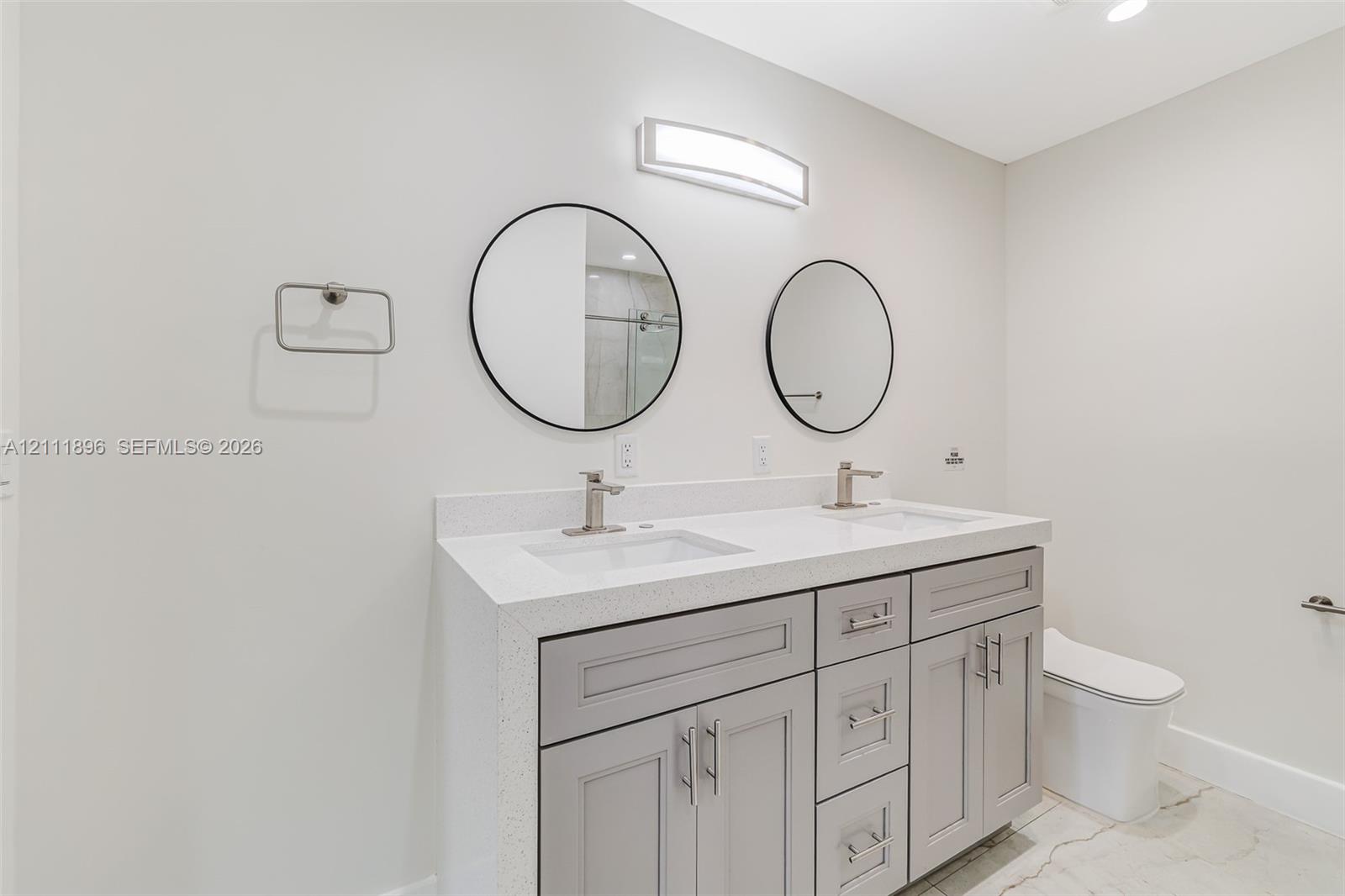 Dual-sink vanity with light gray cabinetry, solid-surface countertop, circular mirrors, and wall-mounted task lighting