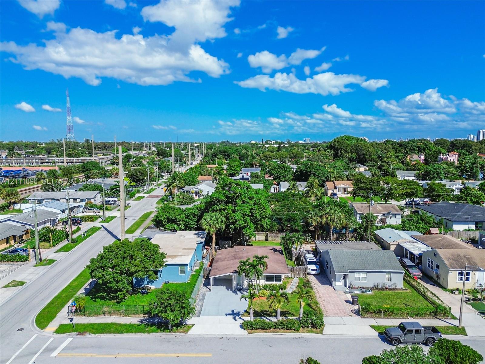 Aerial view of a residential property featuring a paved driveway, covered entryway, and mature palm trees