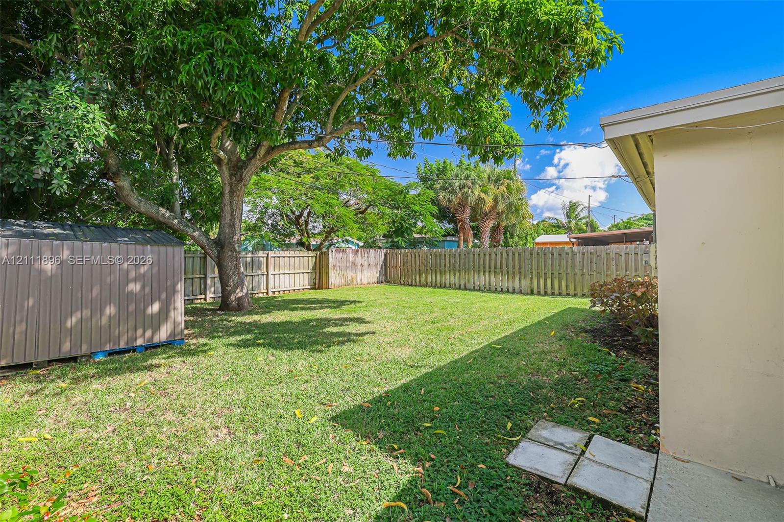 Backyard featuring a grass lawn, mature trees, a detached storage structure, and a wood privacy fence