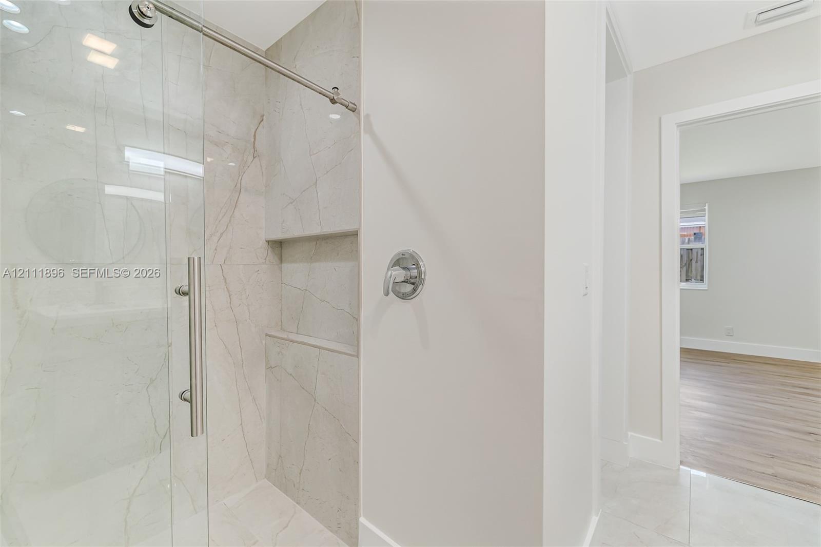 Walk-in shower featuring large-format stone-finish tile surround, a built-in recessed niche, chrome hardware, and a frameless glass enclosure