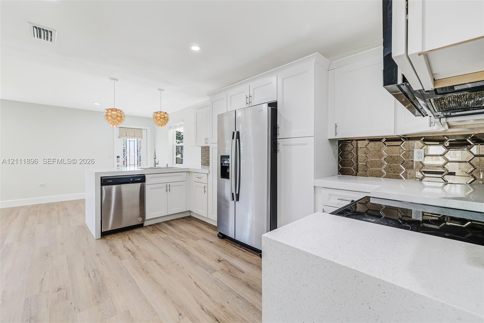 Kitchen featuring white shaker-style cabinetry, quartz countertops, stainless steel appliances, metallic hexagonal tile backsplash, and wood-finish flooring
