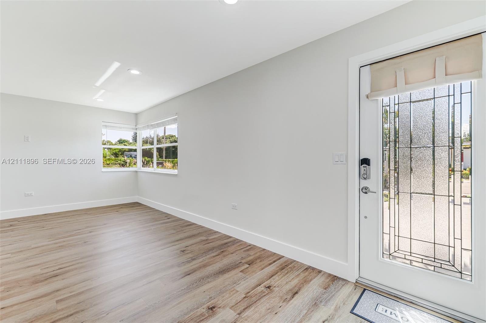 Neutral-toned interior featuring wood-finish flooring, recessed lighting, and a front entry door with a decorative glass insert