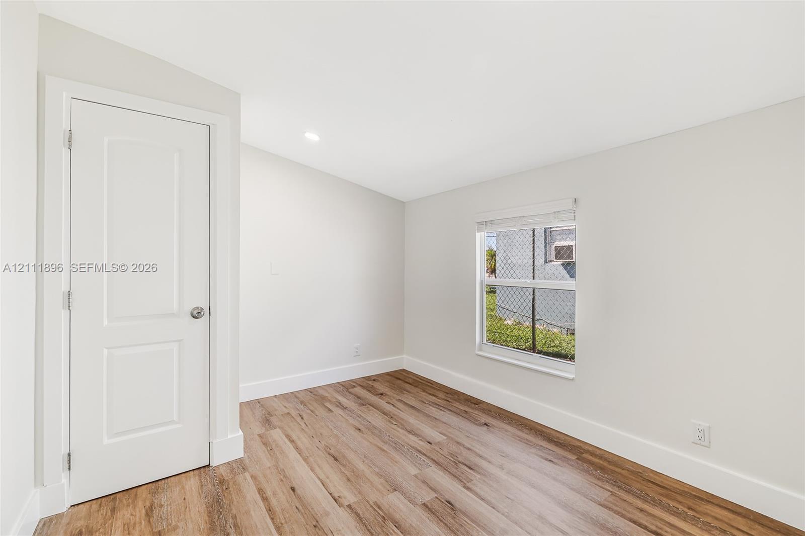 Interior space featuring wood-finish flooring, a recessed ceiling light, a single-pane window, and a white paneled door