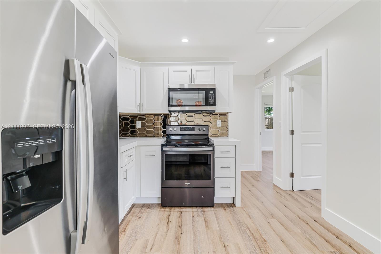 Kitchen featuring white shaker-style cabinetry, stainless steel appliances, honeycomb-patterned backsplash, and wood-finish flooring