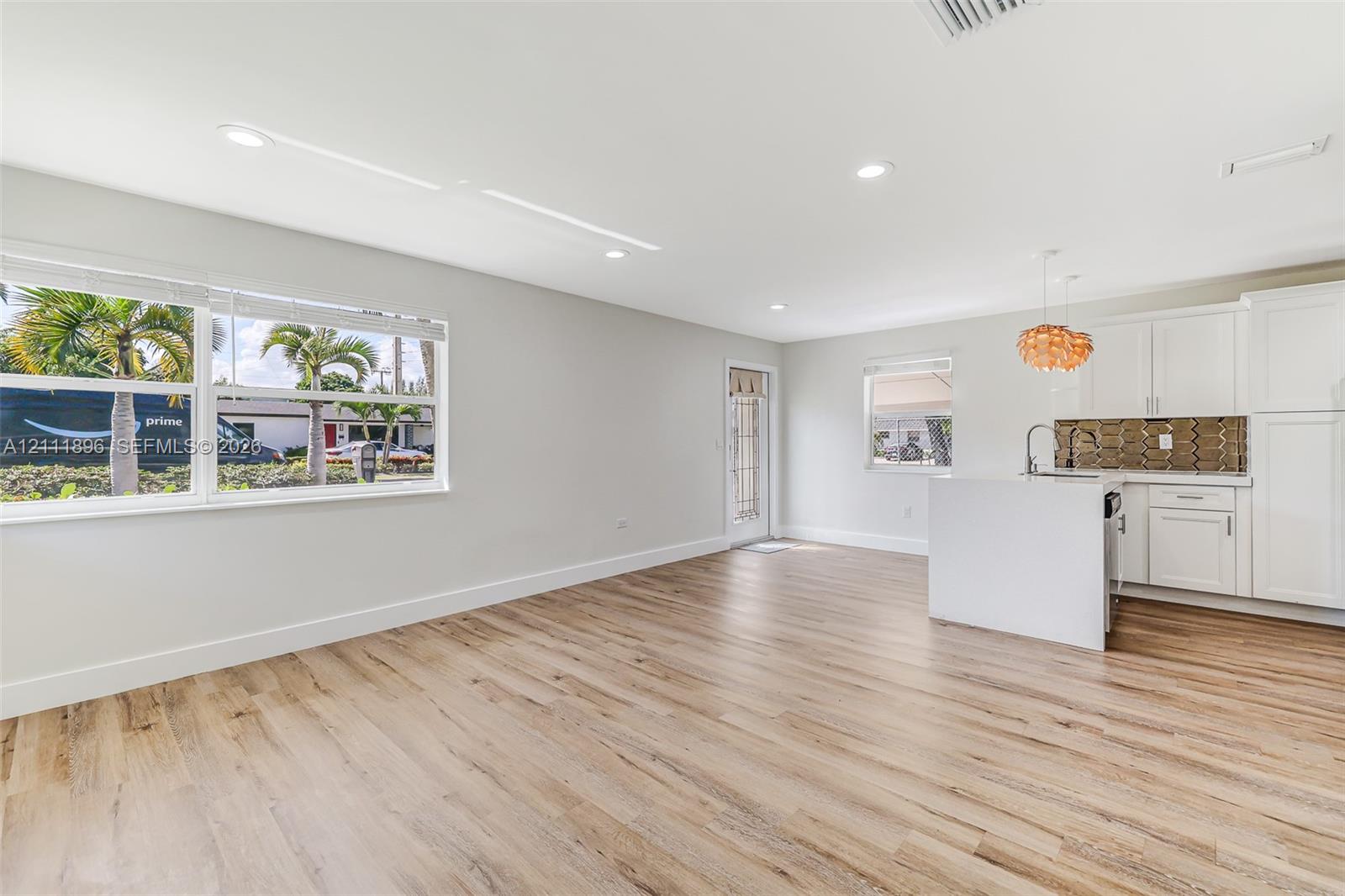 Open-concept living space featuring wood-finish flooring, recessed lighting, white cabinetry, a kitchen island with a built-in sink, and a decorative tile backsplash