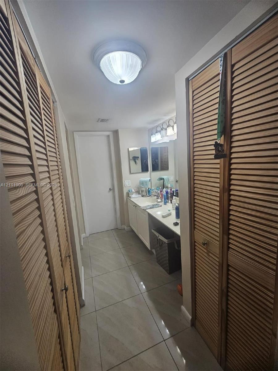 Dual louvered-door closets, tile flooring, vanity with integrated cabinetry, and multi-bulb wall lighting