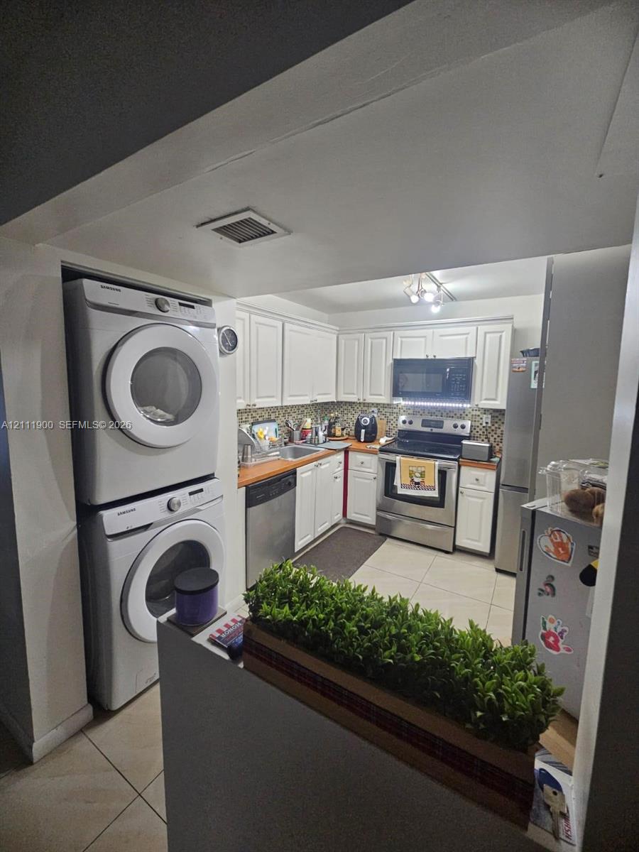 Kitchen featuring white shaker-style cabinetry, stainless steel appliances, tile flooring, and integrated laundry area