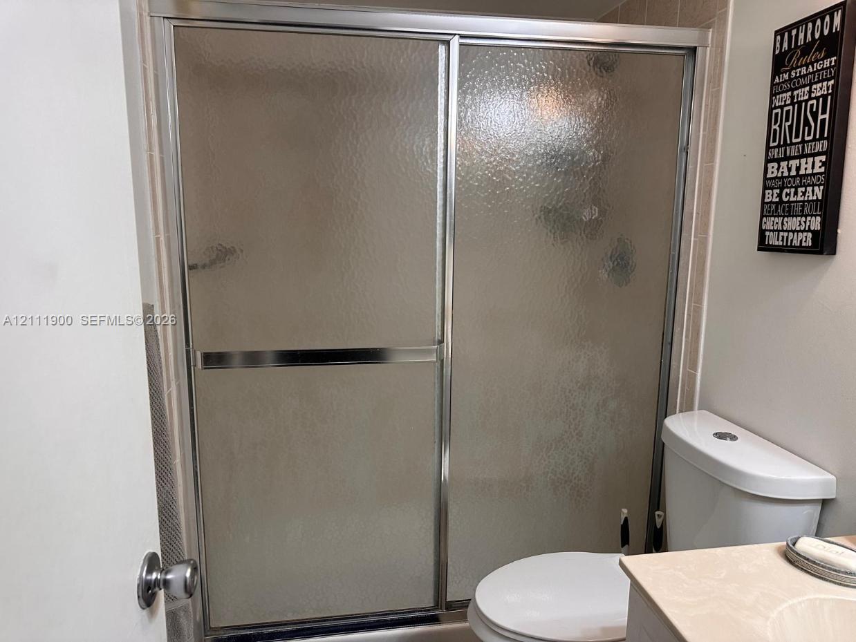 Shower enclosure featuring chrome-finish sliding doors and textured glass, tile surround, and a standard-height toilet