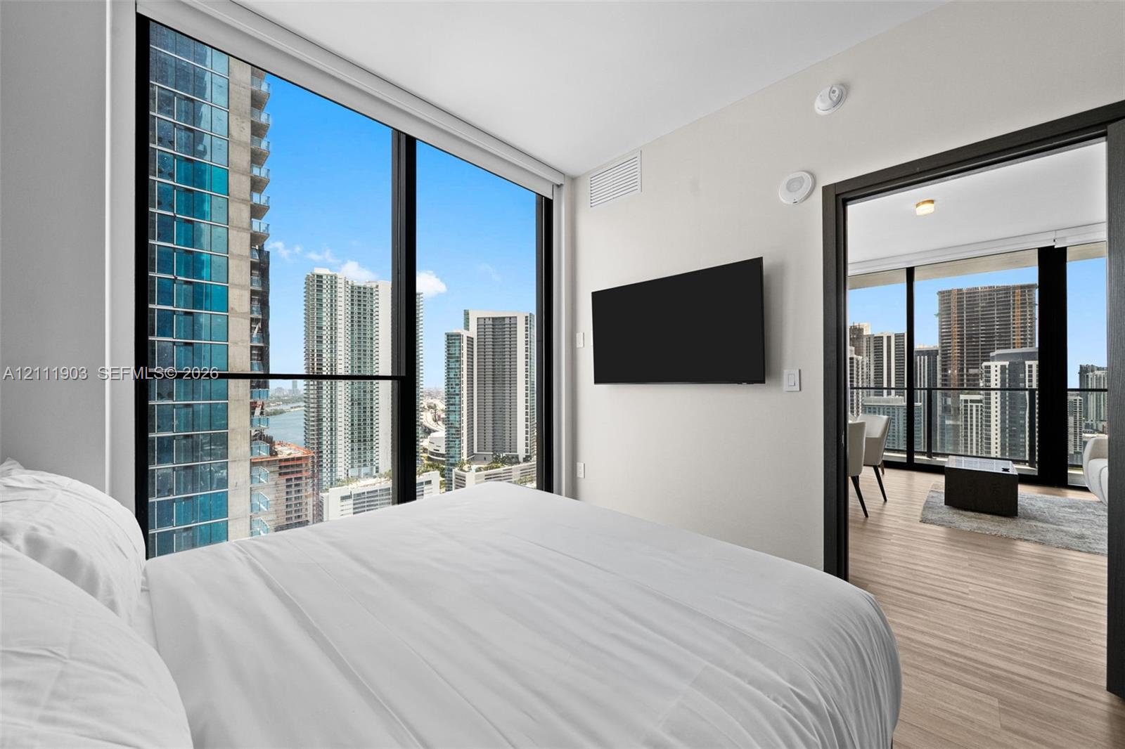Floor-to-ceiling windows, wood-finish flooring, and urban skyline backdrop