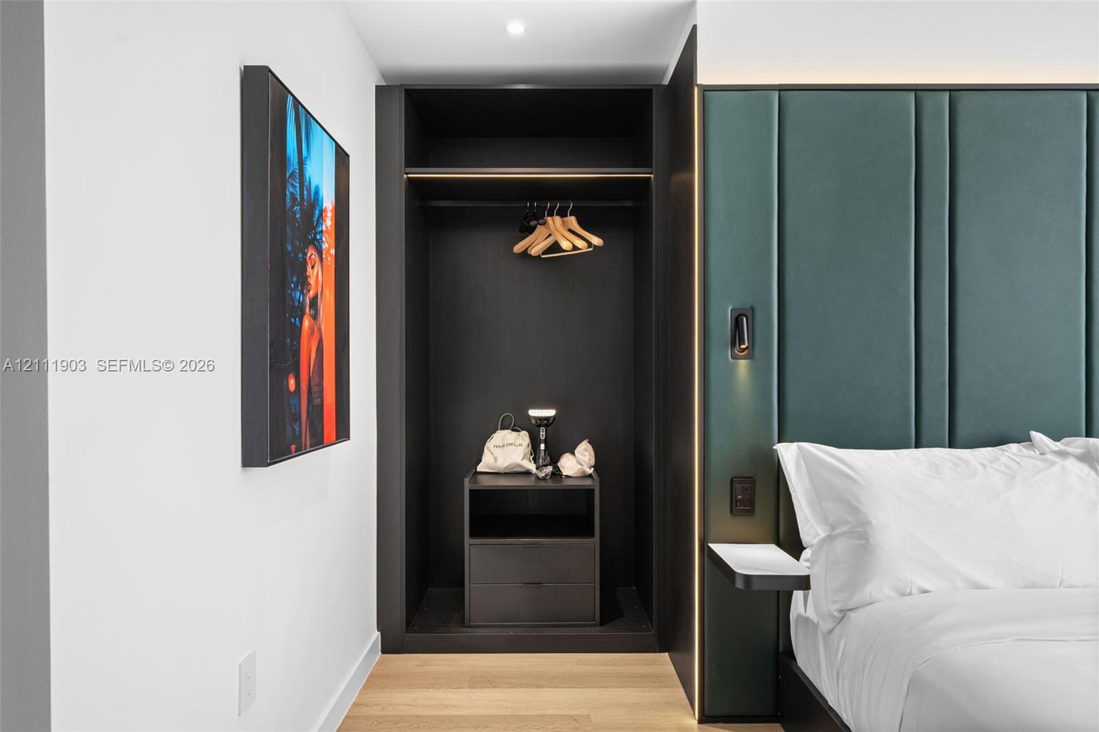 Built-in wardrobe with dark cabinetry, upholstered green vertical-paneled accent wall, recessed lighting, and wood-finish flooring