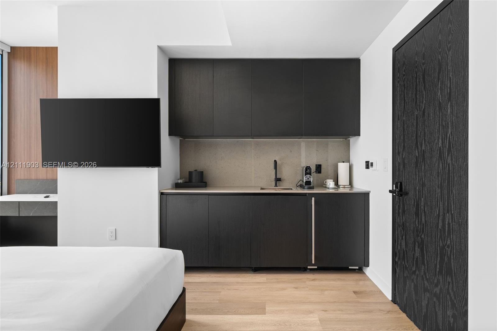 Wet bar featuring matte black cabinetry, stone-finish backsplash, undermount sink with matte black faucet, and built-in under-counter refrigerator