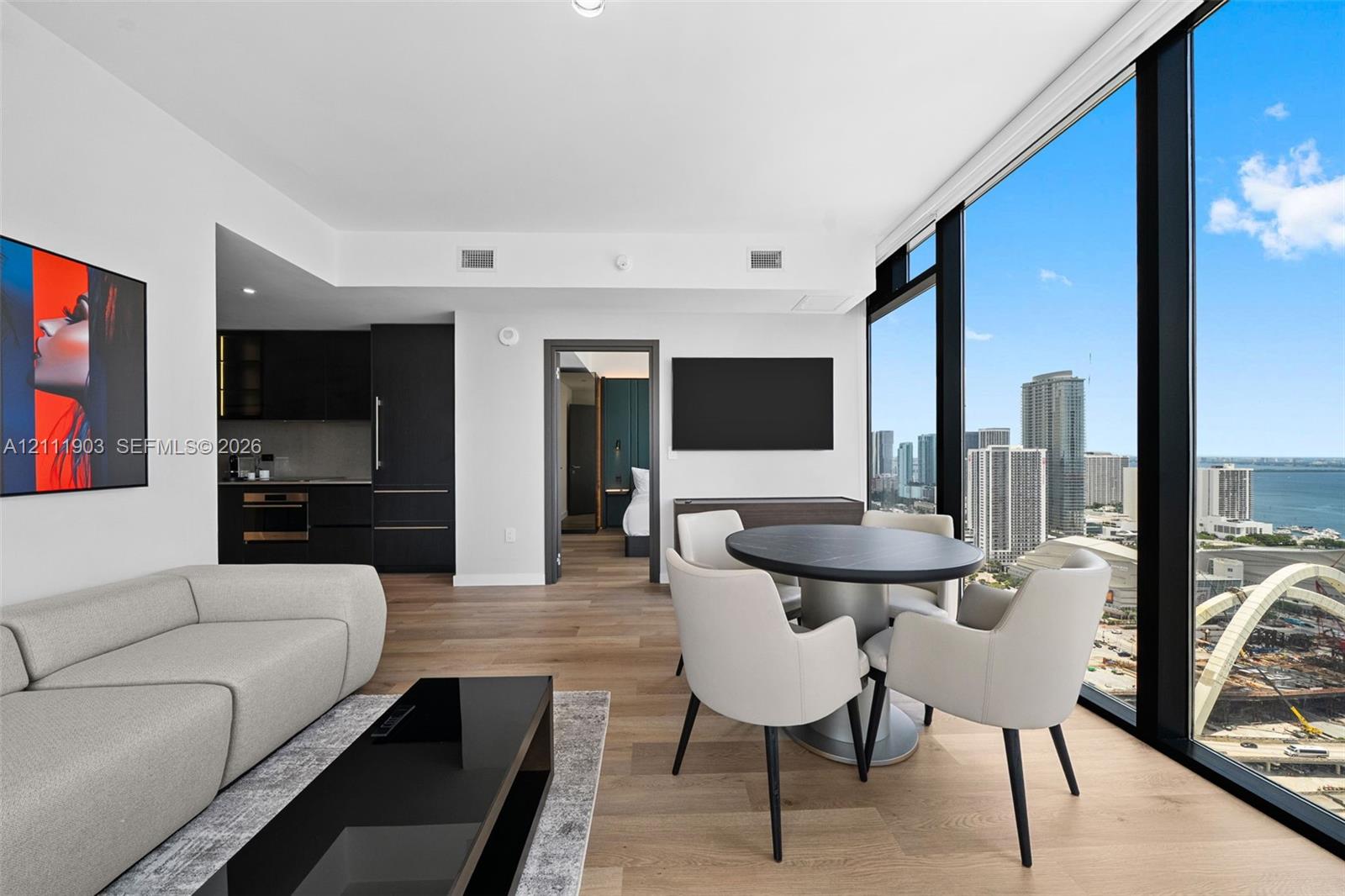 Floor-to-ceiling windows featuring panoramic city and water scenery, wood-finish flooring, and minimalist kitchen cabinetry with integrated appliances