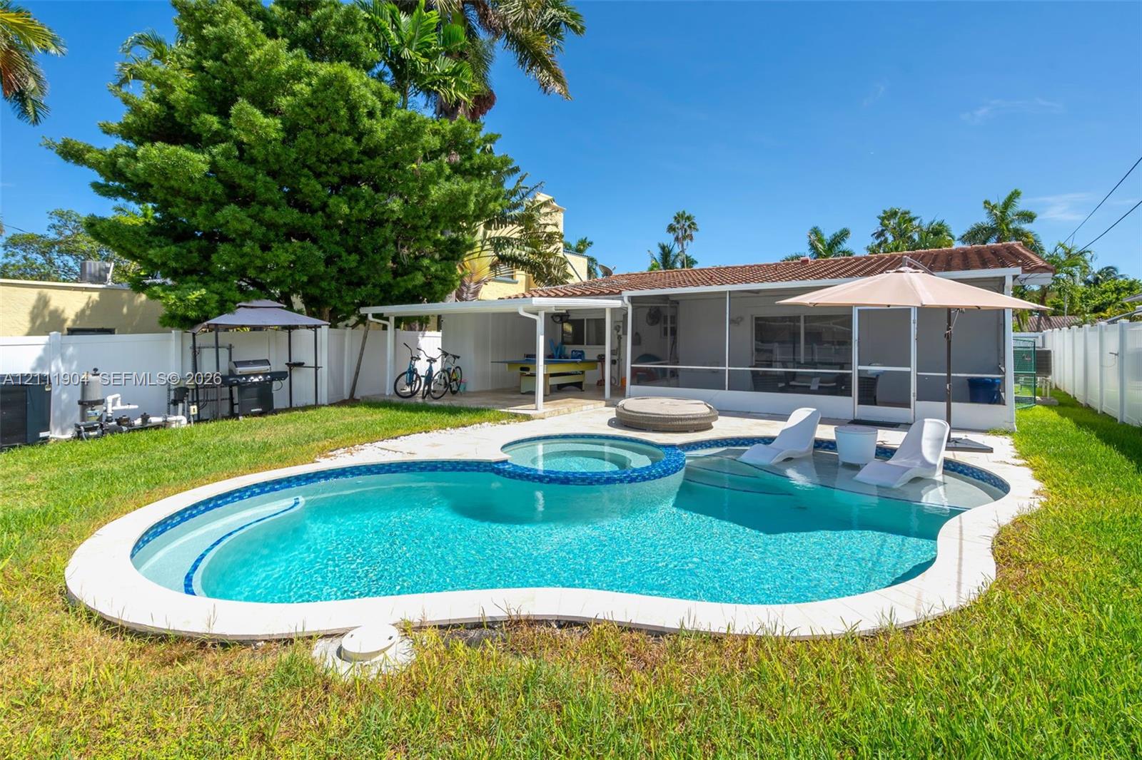 Freeform swimming pool with a built-in spa, integrated sun shelf, screened-in lanai, and a fenced backyard
