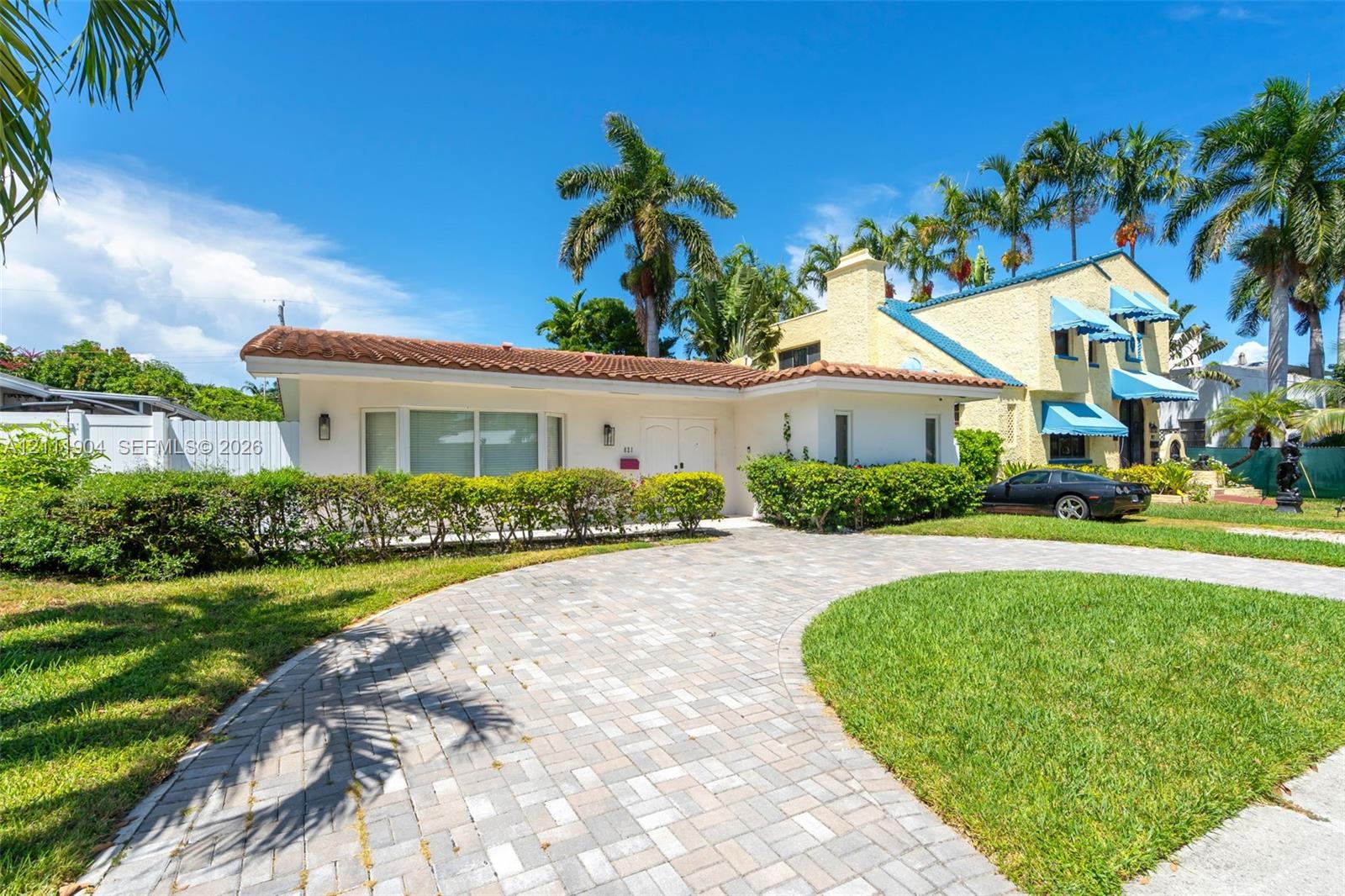 Stucco exterior featuring a terracotta tile roof, brick-paver circular driveway, and manicured landscaping