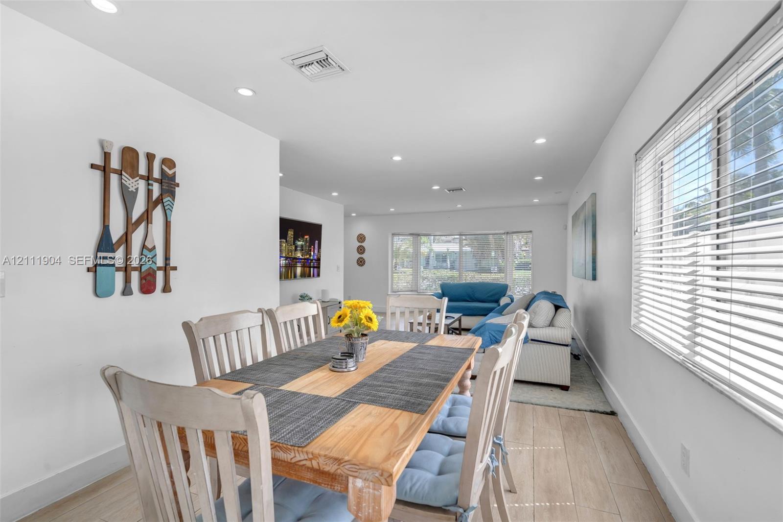 Open-concept living space featuring wood-finish flooring, recessed lighting, and large windows with horizontal blinds
