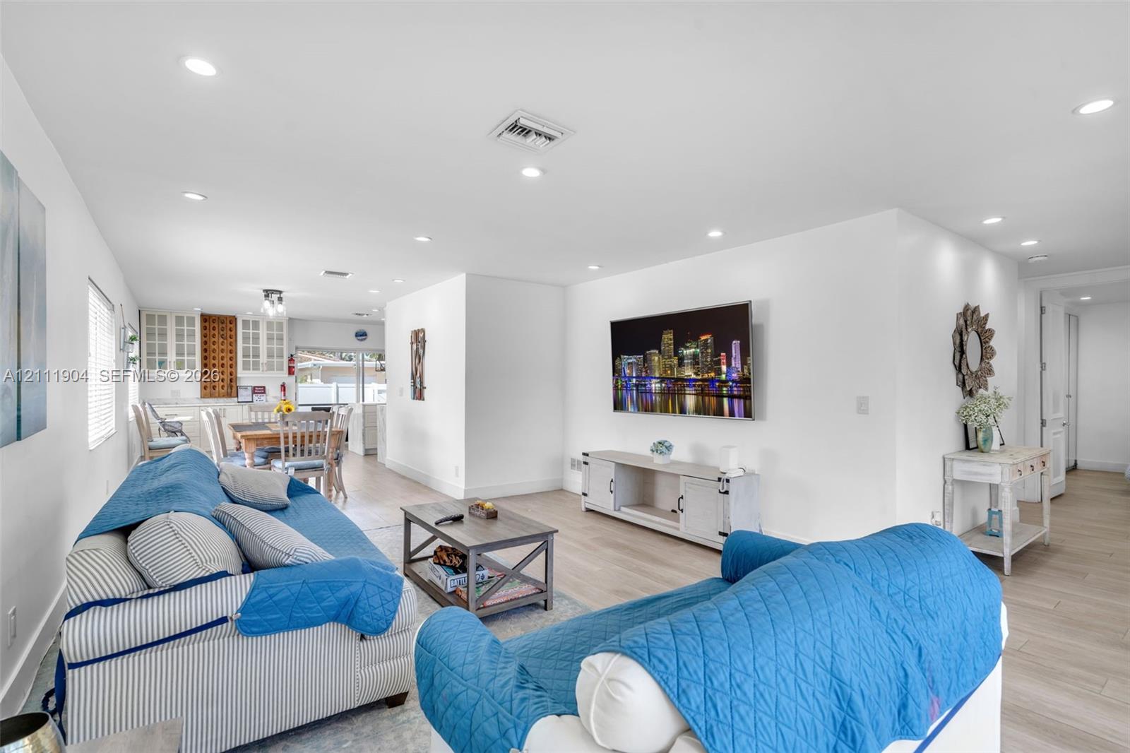 Open-concept interior featuring light-toned wood-finish flooring, recessed lighting, and white cabinetry with glass-front display uppers