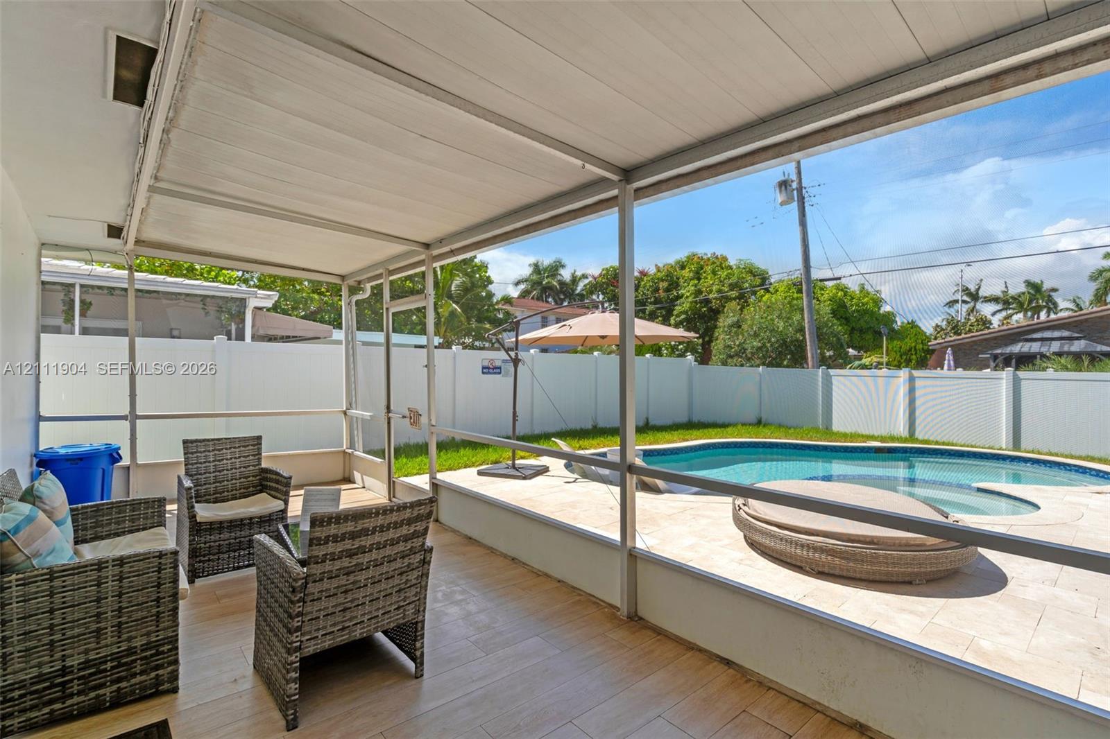 Screened-in lanai featuring wood-finish tile flooring, paved pool deck, custom-shaped swimming pool, and white vinyl privacy fencing