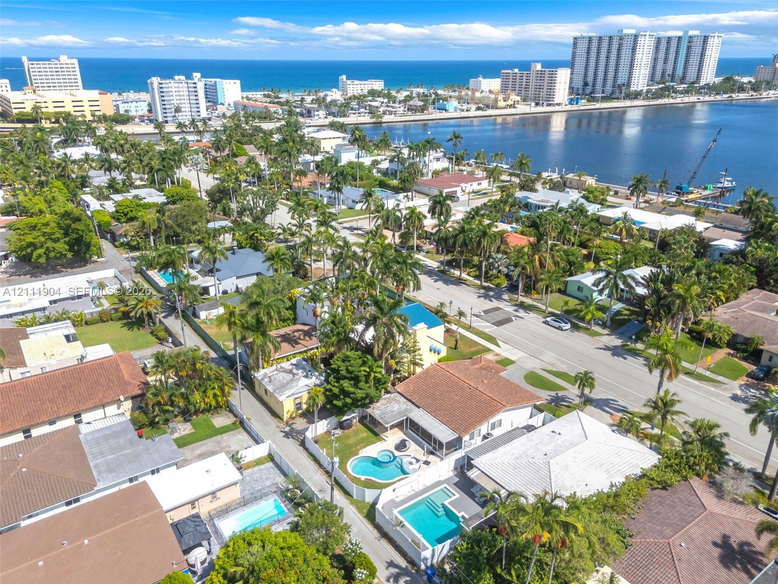 Aerial perspective of a coastal residential neighborhood featuring palm tree-lined streets, proximity to the coastline, and private swimming pools