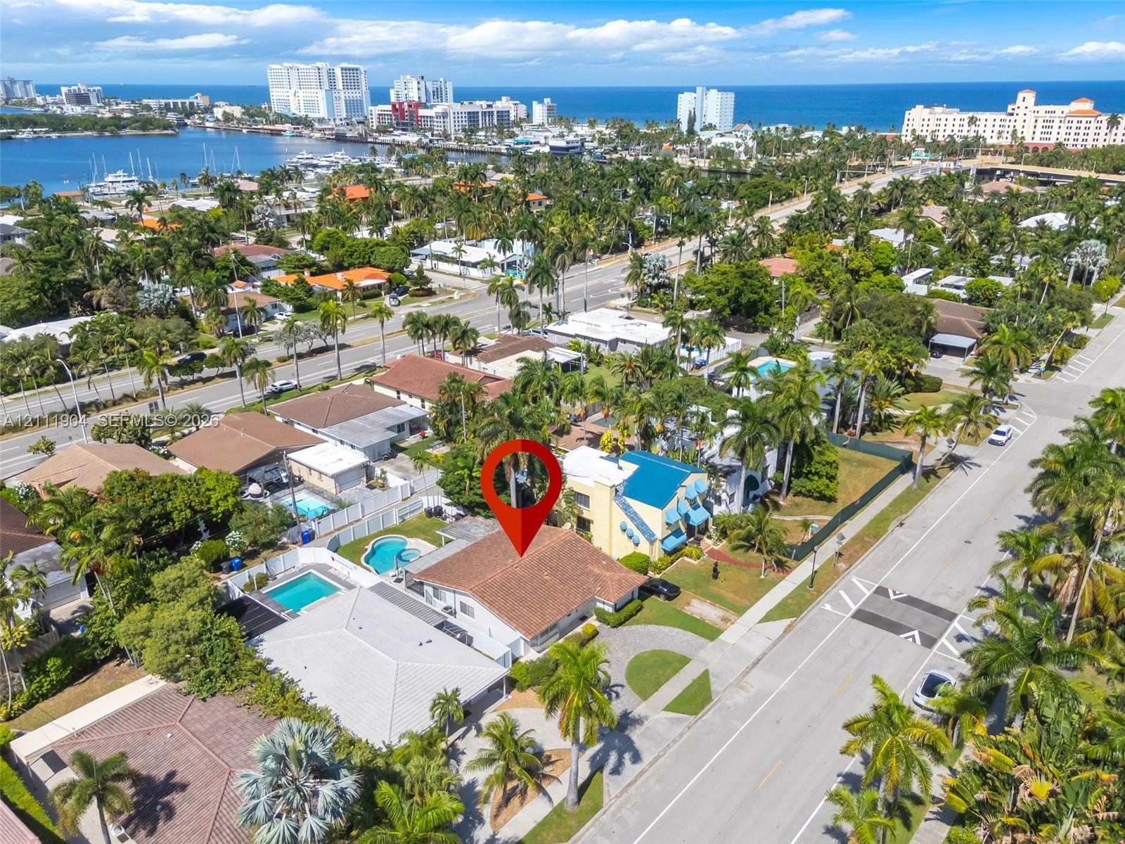 Aerial perspective of a property featuring a multi-pitched roofline, paved driveway, landscaped grounds, and proximity to coastal waterfront and urban centers