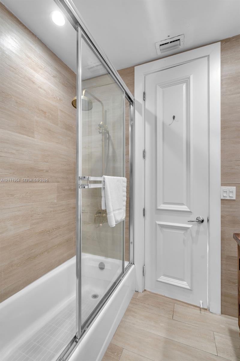 Shower enclosure with sliding glass door, neutral-tone horizontal tile surround, polished metal hardware, and two-panel interior door