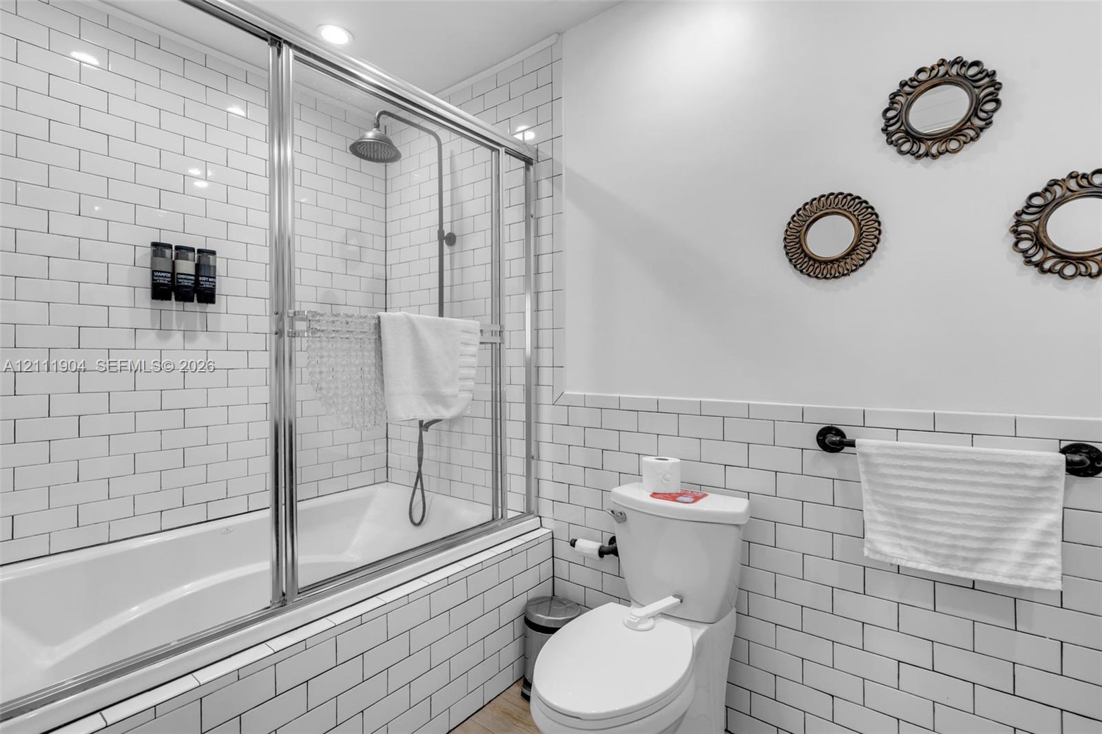 Subway tile wall treatments, chrome-framed glass shower enclosure, deep soaking tub, and wall-mounted metal towel rack