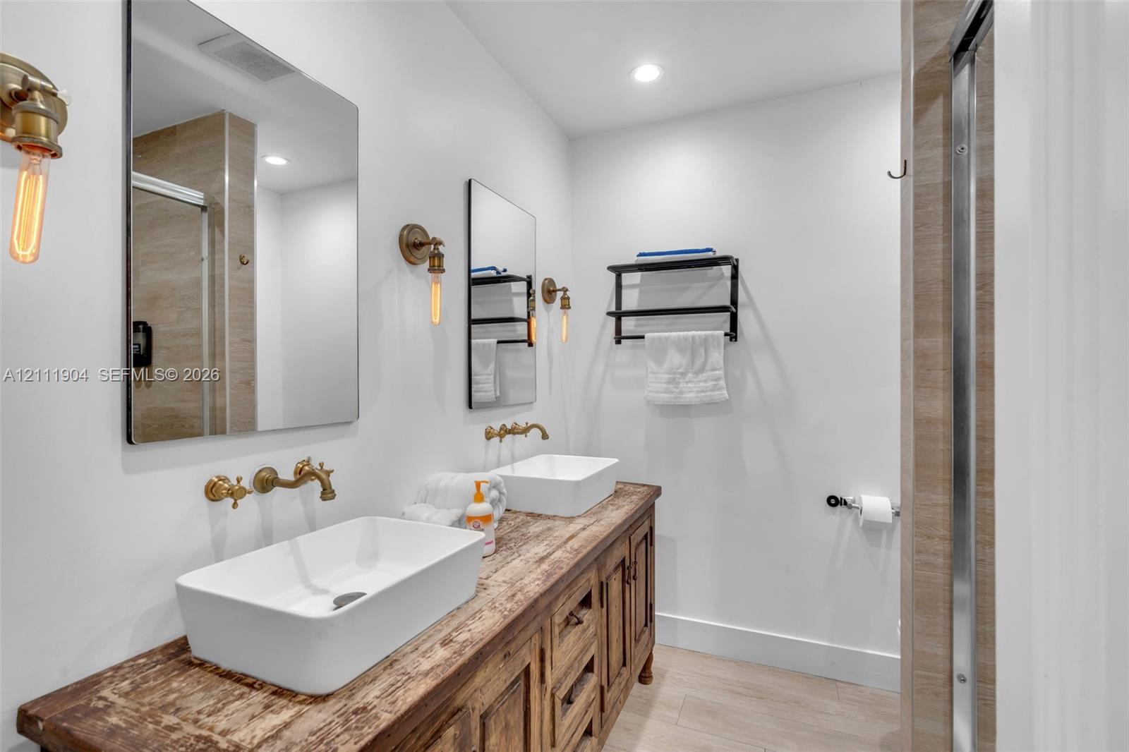 Double vanity featuring a rustic wood-finish cabinet, rectangular vessel sinks, wall-mounted brass faucets, and industrial-style Edison bulb light fixtures