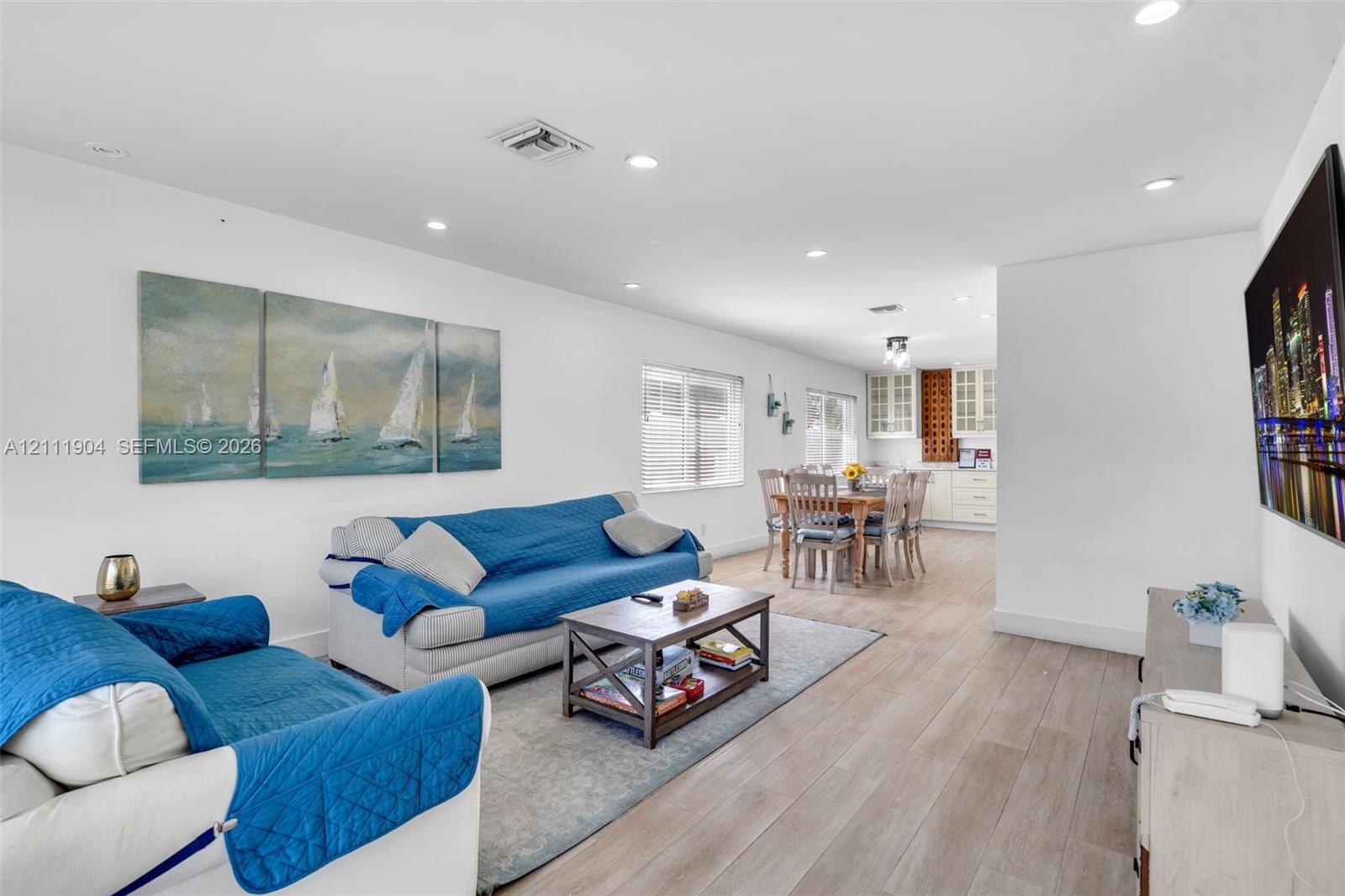 Open-concept interior featuring wood-finish flooring, recessed lighting, and white cabinetry with glass-front uppers