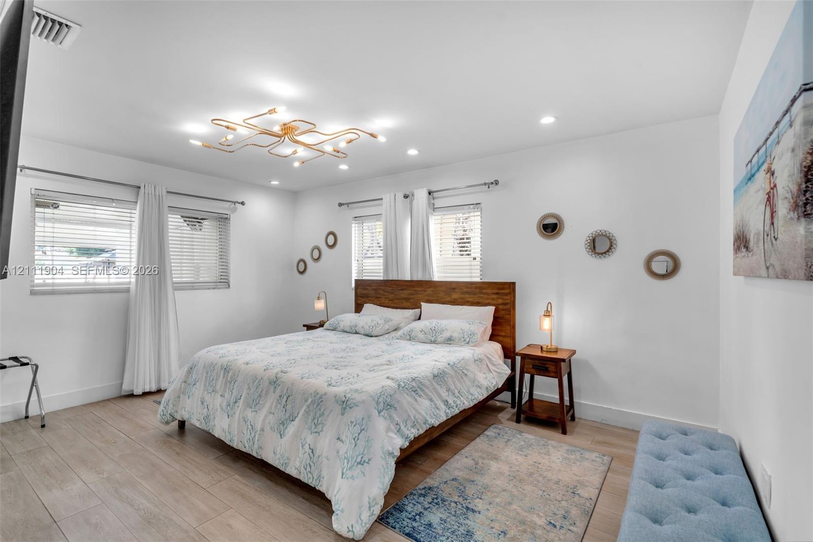 Room featuring wood-finish flooring, recessed lighting, a modern geometric ceiling fixture, and dual windows with horizontal blinds