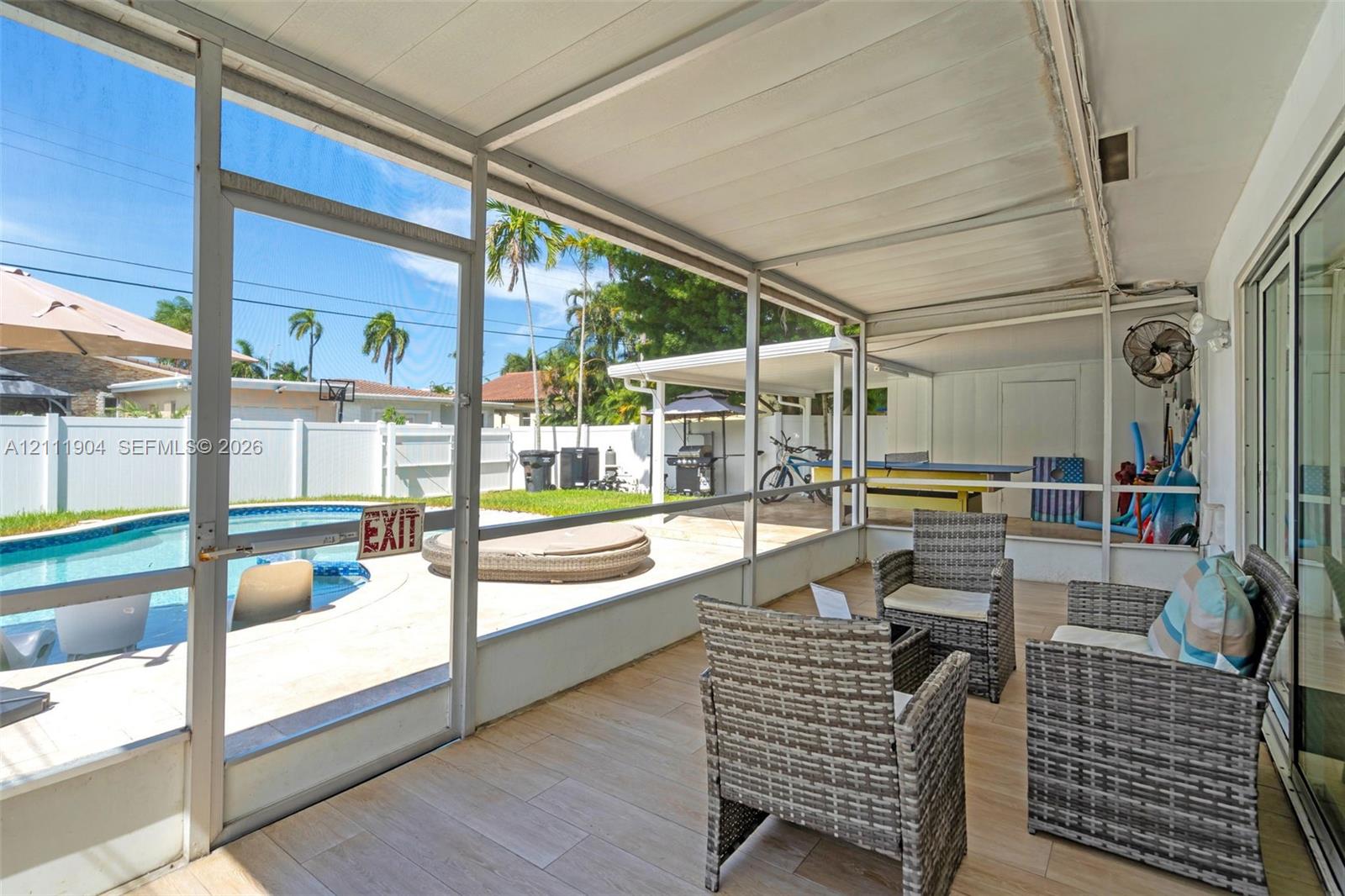 Screened-in lanai featuring wood-finish tile flooring, a metal frame enclosure, and a direct entrance to an outdoor swimming pool and concrete patio area