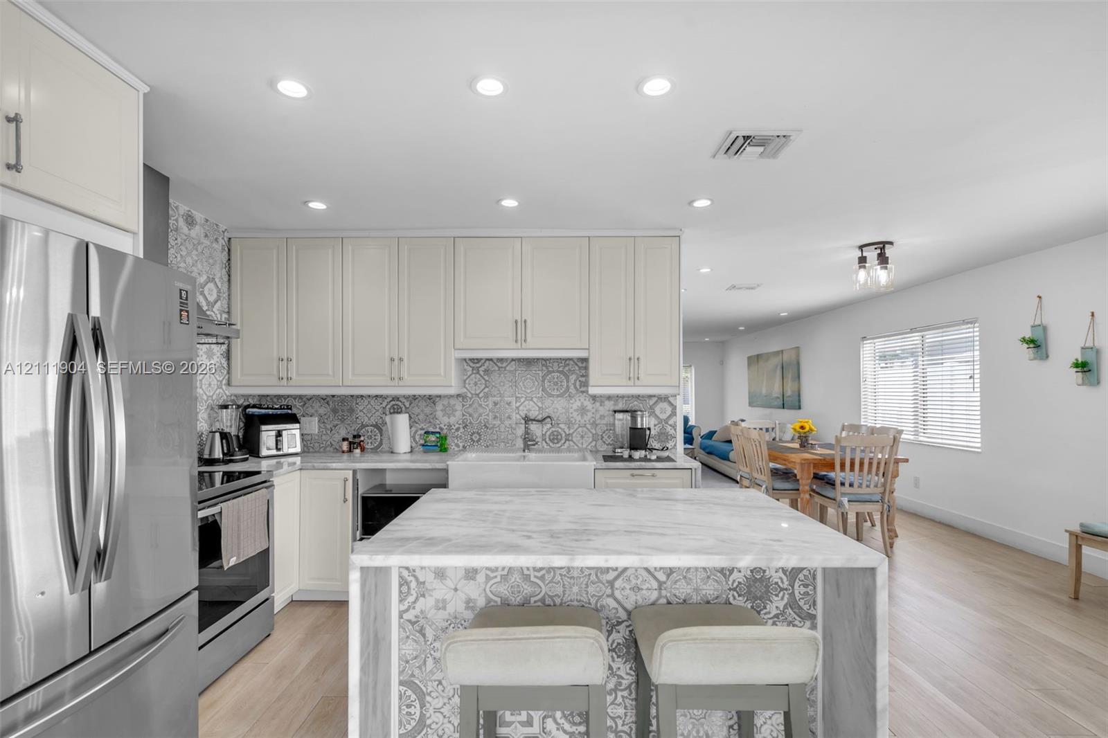 Kitchen featuring light-toned cabinetry, patterned tile backsplash, central island with a stone-finish countertop, stainless steel refrigerator, and wood-finish flooring