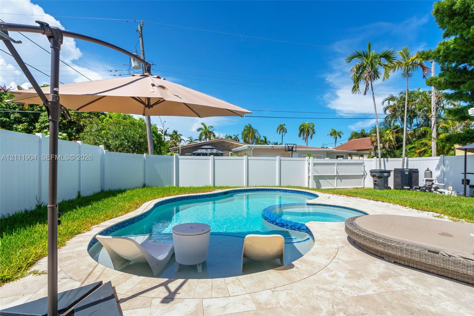 Private backyard featuring an in-ground pool with integrated spa, light-toned stone pool decking, and white vinyl privacy fencing
