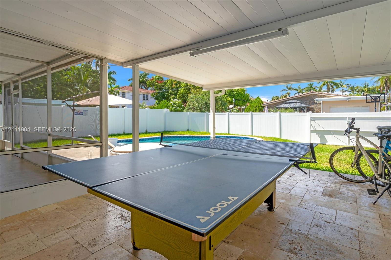 Covered screened-in patio featuring stone-tile flooring and a white vinyl perimeter fence enclosing an outdoor pool