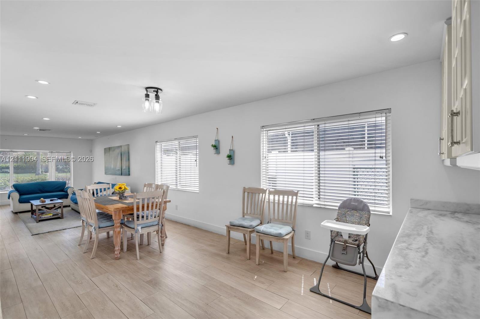 Open-concept space featuring wood-finish flooring, recessed lighting, expansive windows with horizontal blinds, and stone-finish countertops